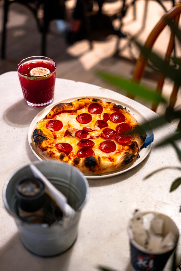 Delicious pepperoni pizza served with a refreshing drink in an outdoor setting.